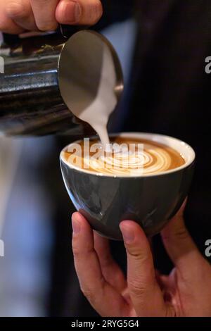 Barista che prepara il caffè latte, versando il latte in un caffè. Primo piano sulle mani con la latte art. Foto Stock
