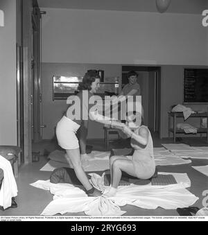 Ginnastica in passato. In una palestra, un gruppo di donne si inginocchiano e allungano le braccia in un movimento. Le giovani donne si prendono una pausa dal lavoro e fanno ginnastica durante l'orario di lavoro. La ginnastica da ufficio era un'invenzione moderna negli anni '1940, quando l'assistenza sanitaria per i dipendenti cominciò ad essere implementata. Svezia 1949. Kristoffersson rif. AX72-6 Foto Stock