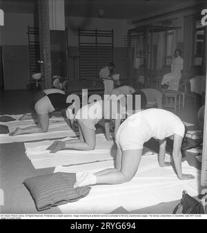 Ginnastica in passato. In una palestra, un gruppo di donne si inginocchiano e allungano le braccia in un movimento. Le giovani donne si prendono una pausa dal lavoro e fanno ginnastica durante l'orario di lavoro. La ginnastica da ufficio era un'invenzione moderna negli anni '1940, quando l'assistenza sanitaria per i dipendenti cominciò ad essere implementata. Svezia 1949. Kristoffersson rif. AX72-6 Foto Stock