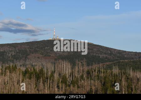 La torre radio e gli edifici sulla cima del monte Brocken sotto il cielo blu e i fitti alberi morti mangiati dai coleotteri della corteccia nell'H Foto Stock