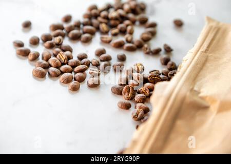 Chicchi di caffè tostati versati dal sacchetto di carta sul tavolo di marmo, primo piano macro shot Foto Stock