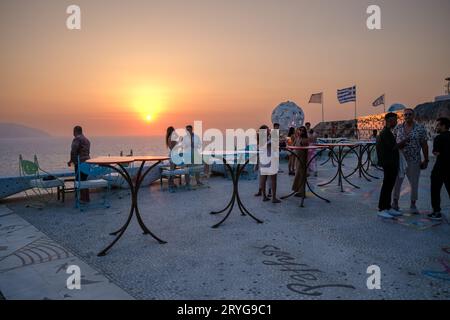 IOS, Grecia - 8 settembre 2023: I turisti si godono un drink e una vista mozzafiato sul Mar Egeo con un tramonto arancione in un lounge bar in Grecia Foto Stock