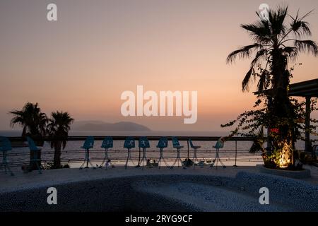 IOS, Grecia - 8 settembre 2023: Vista di un lounge bar all'aperto con palme e una piscina, affacciato sul Mar Egeo e di uno splendido tramonto Foto Stock