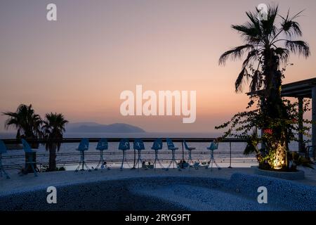 IOS, Grecia - 8 settembre 2023: Vista di un lounge bar all'aperto con palme e una piscina, affacciato sul Mar Egeo e di uno splendido tramonto Foto Stock