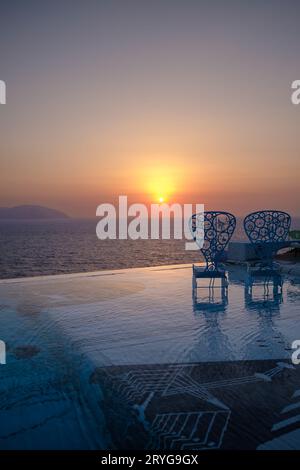 IOS, Grecia - 8 settembre 2023: Vista di due sedie decorate in una piscina che si affaccia sul Mar Egeo e di un bellissimo tramonto a iOS Grecia Foto Stock