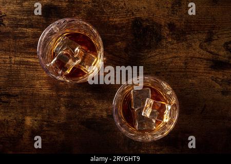 Whisky in bicchieri con ghiaccio. Whisky al bourbon sulle rocce su un fondo di legno rustico scuro, sparato piatto sopra la testa Foto Stock