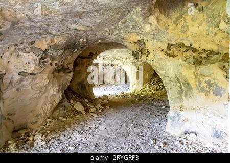 Tunnel all'interno di una grotta vuota, pareti con struttura irregolare e crepe, pietre su terreno sabbioso sullo sfondo, riserva naturale Thier de Lanaye nella Belgia Foto Stock