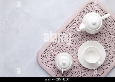 Tè mattutino. Teiera in ceramica bianca, tazza e ciotola da zucchero su un vassoio rosa aperto Sfondo in marmo grigio. Impostazione del piano d'esame, piano d'esame, vista dall'alto. Servin Foto Stock