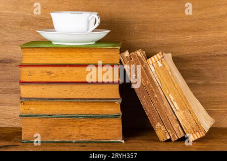 Pila di vecchi libri e una tazza di caffè su un tavolo di legno. Foto Stock