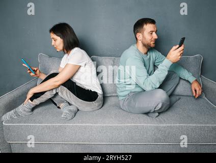 Una giovane coppia annoiata seduta sul divano a guardare i loro smartphone Foto Stock
