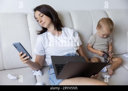 una giovane mamma sta cercando di lavorare a casa con un bambino. Procrastinazione sul lavoro. Foto Stock