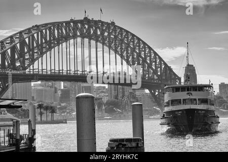 Foto in bianco e nero dell'iconico Manly Ferry, MV COLLAROY che si avvicina al molo a Circular Quay, lo storico Sydney Harbour Bridge sullo sfondo Foto Stock