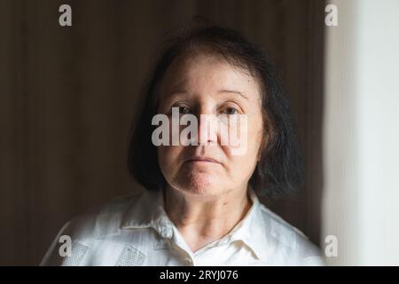 Ritratto di una donna anziana in piedi accanto alla finestra Foto Stock