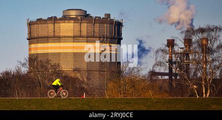 Ciclisti sulla diga del Reno di fronte alla ThyssenKrupp Steel Industry, Duisburg, Germania, Europa Foto Stock