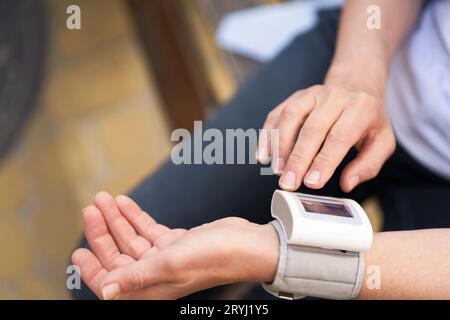 Primo piano delle mani di una donna anziana che tiene il dispositivo di misurazione della pressione all'aperto. L'immagine rappresenta il concetto di monitor dello stato Foto Stock