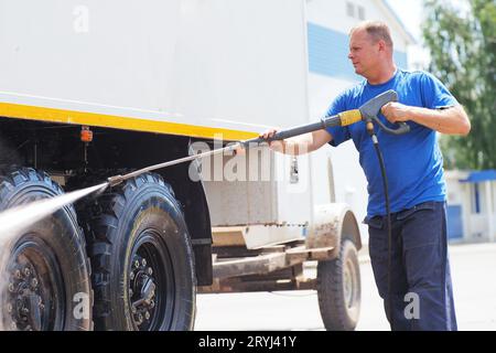 Autolavaggio per veicoli pesanti e cargo. Il lavavetri maschio in lava un camion con una pistola ad acqua in strada in un giorno d'estate. Foto Stock