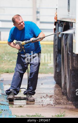 Autolavaggio per veicoli pesanti e cargo. Il lavavetri maschio in lava un camion con una pistola ad acqua in strada in un giorno d'estate. Foto Stock