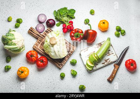 Verdure fresche varie con taglieri in legno e coltello sul tavolo da cucina bianco vista dall'alto. Cucina vegetariana con ingredienti sani, dieta Foto Stock