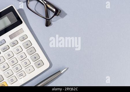 Piatto di calcolatrice, penna e occhiali su sfondo grigio con Copy Space Foto Stock