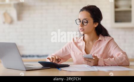 Giovane commercialista europea che lavora da casa, utilizzando computer portatile, cellulare e calcolatrice, panorama, spazio fotocopie Foto Stock