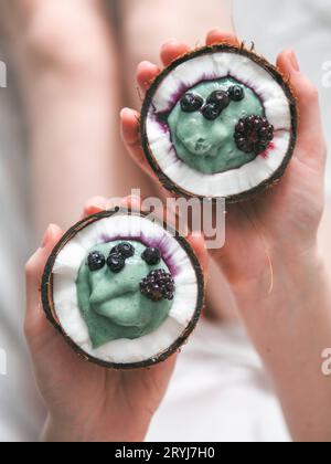 Due metà di noce di cocco spirulina smoothie nelle mani della donna Foto Stock
