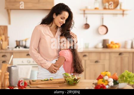 La mamma ama abbracciare la figlia mentre cucina insieme in una cucina moderna Foto Stock