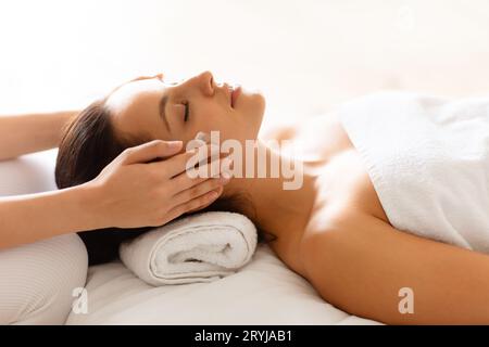 Mani che massaggiano la testa della donna e i templi al salone termale, primo piano Foto Stock