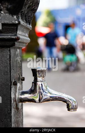 Rubinetto d'acqua pubblico all'aperto nel centro di Londra con una famiglia sfocata che indossa abiti colorati sullo sfondo luglio 2010 Foto Stock