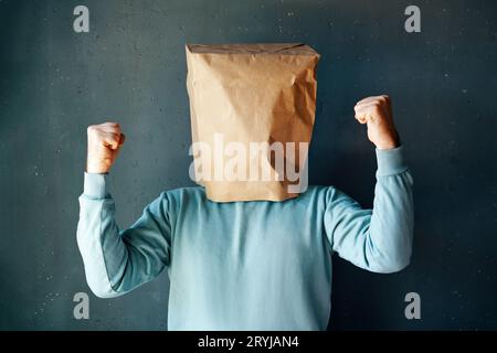 Uomo felice con un sacchetto di carta in testa che celebra il suo successo con il gesto del vincitore Foto Stock