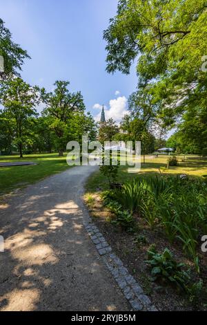 Lungo percorso sinuoso in un bellissimo parco verde con torre di edifici al mattino soleggiato con cielo blu e poche nuvole bianche Foto Stock