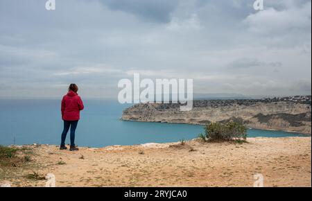 Donna turistica non riconosciuta che si trova ai margini della collina e che si gode il panorama di una costa rocciosa Foto Stock