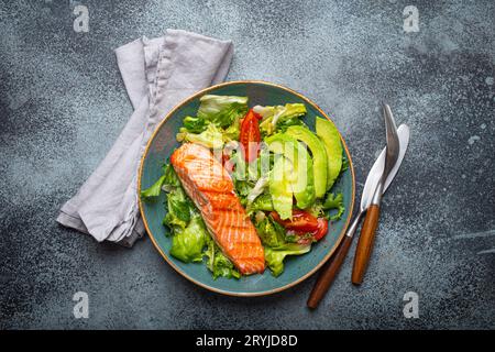 Pesce alla griglia, insalata di salmone e verdure con avocado su piatto di ceramica su sfondo rustico in pietra, vista dall'alto, dieta bilanciata, Foto Stock