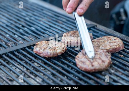 Lo chef prepara carne di hamburger presso il ristorante all'aperto grill. Festival food, fast food, polpette di carne alla griglia con le pinze in mano. Hig Foto Stock