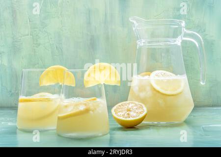 Limonata. Acqua di limone bere con ghiaccio, due bicchieri e una caraffa su sfondo blu. Disintossicare la bevanda. Cocktail appena fatto in casa Foto Stock