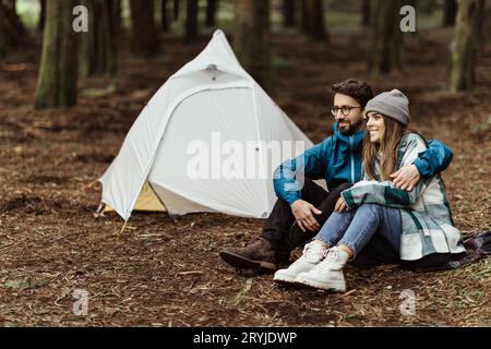 Felice giovane famiglia caucasica in giacche sedute, rilassarsi vicino alla tenda, godersi l'avventura, tempo libero Foto Stock