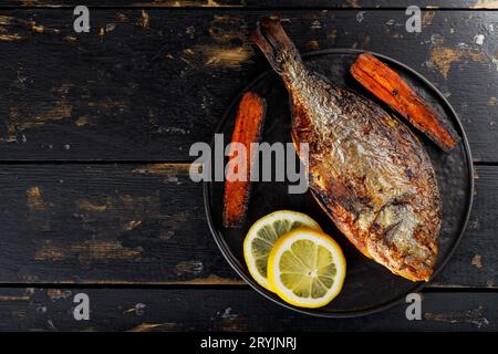 Pesce dorado fritto con verdure alla griglia e limone su un vecchio tavolo di legno. Vista dall'alto. Copia spazio Foto Stock