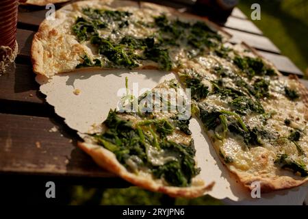 Tarte flambée alsaziana con spinaci e formaggio su un tavolo in un ristorante birreria all'aperto, una fetta è stata mangiata Foto Stock