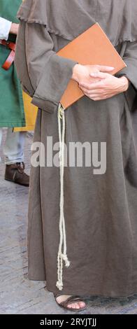 Frate francescano con il lungo abito marrone chiamato Habit e la corda intorno alla vita con il libro sacro a portata di mano e i sandali ai piedi Foto Stock