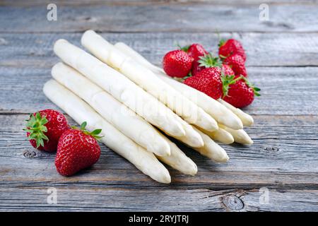 Fragole rosse mature e asparagi bianchi da agricoltura biologica offerti da vicino su un vecchio e rustico asse di legno Foto Stock