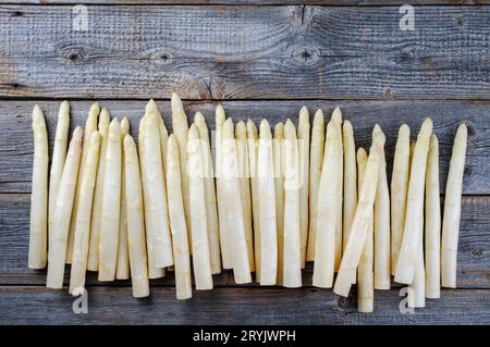 Asparagi bianco grezzo con perline in fila come vista dall'alto con spazio per la copia sulla parte superiore su un pannello di legno grigio sbiancato Foto Stock