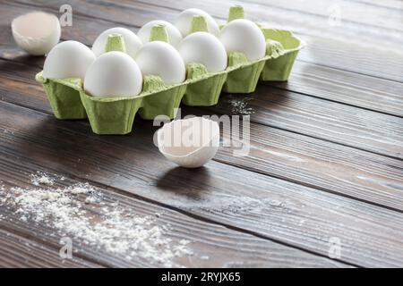 Uova di gallina in scatola, guscio d'uovo, uovo rotto in piatto, frusta metallica. Sfondo di legno scuro. Copia spazio Foto Stock