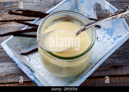 Salsa tradizionale alla vaniglia bourbon con fagioli da vicino in un barattolo su un vassoio di legno Foto Stock