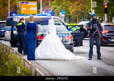 Hannover, Germania. 1 ottobre 2023. Gli agenti di polizia controllano i partecipanti a una processione nuziale e i loro veicoli. I passanti hanno riferito di aver udito degli spari provenienti dalle auto la domenica sera e hanno chiamato il 110. Otto auto sono state perquisite, ma alla fine non è stato trovato nulla. Gli ospiti del matrimonio hanno dovuto lasciare le loro limousine - anche la sposa ha dovuto aspettare su una strada principale a otto corsie nel centro della città con il suo opulento vestito bianco per finire le perquisizioni della polizia Credito: Moritz Frankenberg/dpa - ATTENZIONE: Le persone sono state pixelate per motivi di privacy/dpa/Alamy Live News Foto Stock