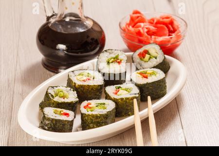 Involtini di sushi con riso, verdure e frutti di mare su piatto con bottiglia di salsa di soia. Foto Stock