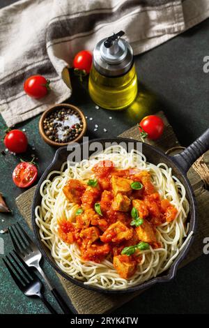 Cibo sano, pasta italiana. Spaghetti con pollo e verdure in salsa di pomodoro in una padella di ghisa su un piano di pietra. Foto Stock