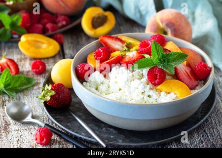 Colazione estiva rustica o dessert. Formaggio di cagliata o di cottage servito con frutta fresca estiva e frutti di bosco su un tavolo di legno. Foto Stock