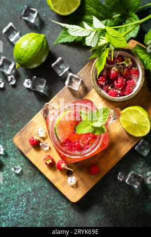 Bevande estive, bevande analcoliche da bar. I bicchieri rinfrescanti bevono lamponi con lime alla menta e ghiaccio su un tavolo in pietra scura. Vista dall'alto piatta Foto Stock