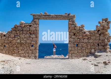 Giovane donna vestita all'uncinetto alla porta di pietra a Paralia Firopotamos, Milos Foto Stock