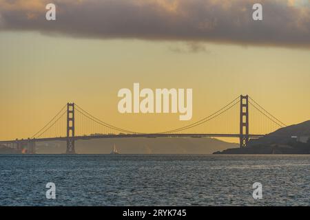 Golden Gate Bridge che sorge in lontananza al tramonto con la barca a vela sottostante Foto Stock