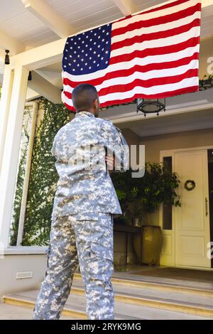 Biracial maschio soldato americano indossando uniforme militare guardando la bandiera degli stati uniti fuori dalla casa Foto Stock